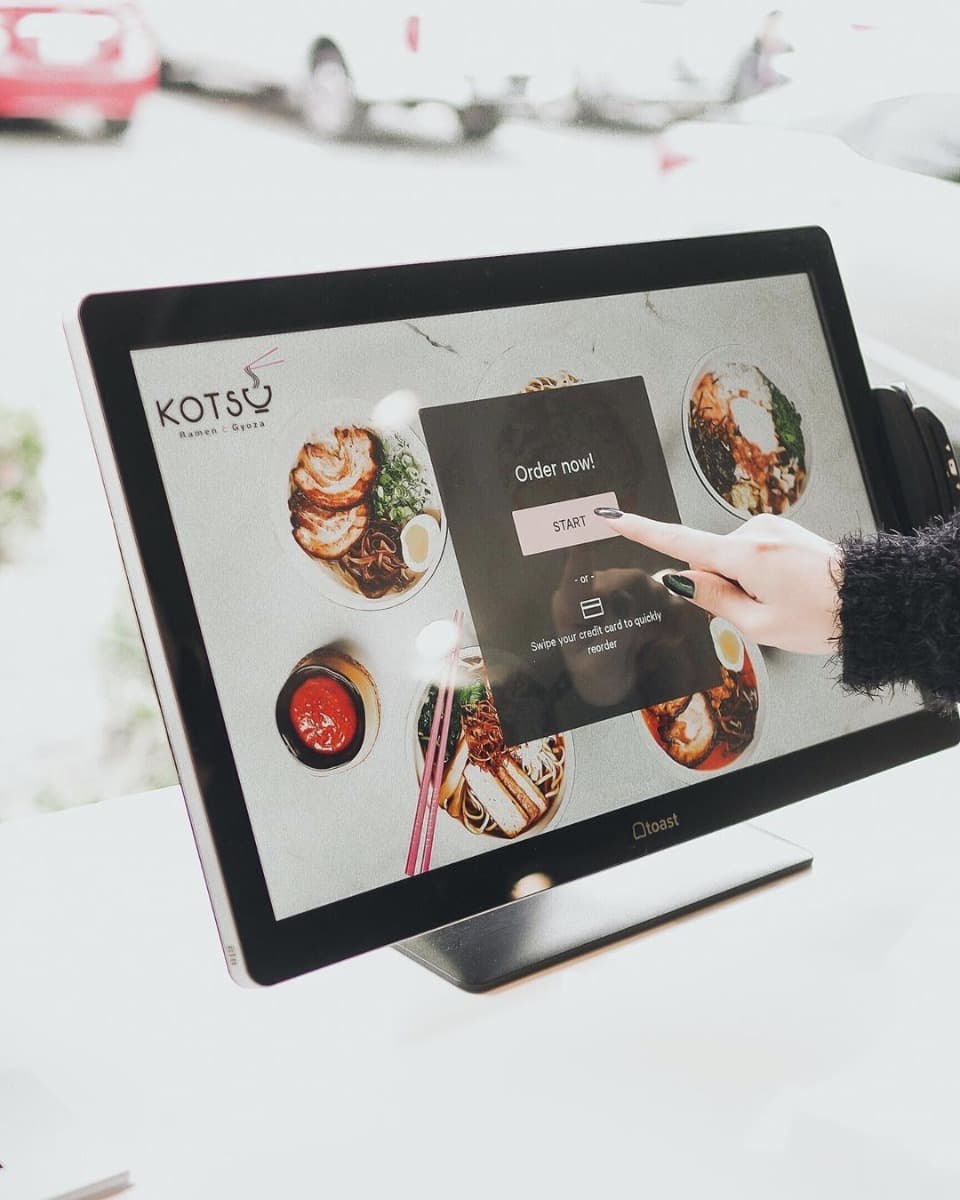 A guest using the ordering kiosk beside bowls of ramen
