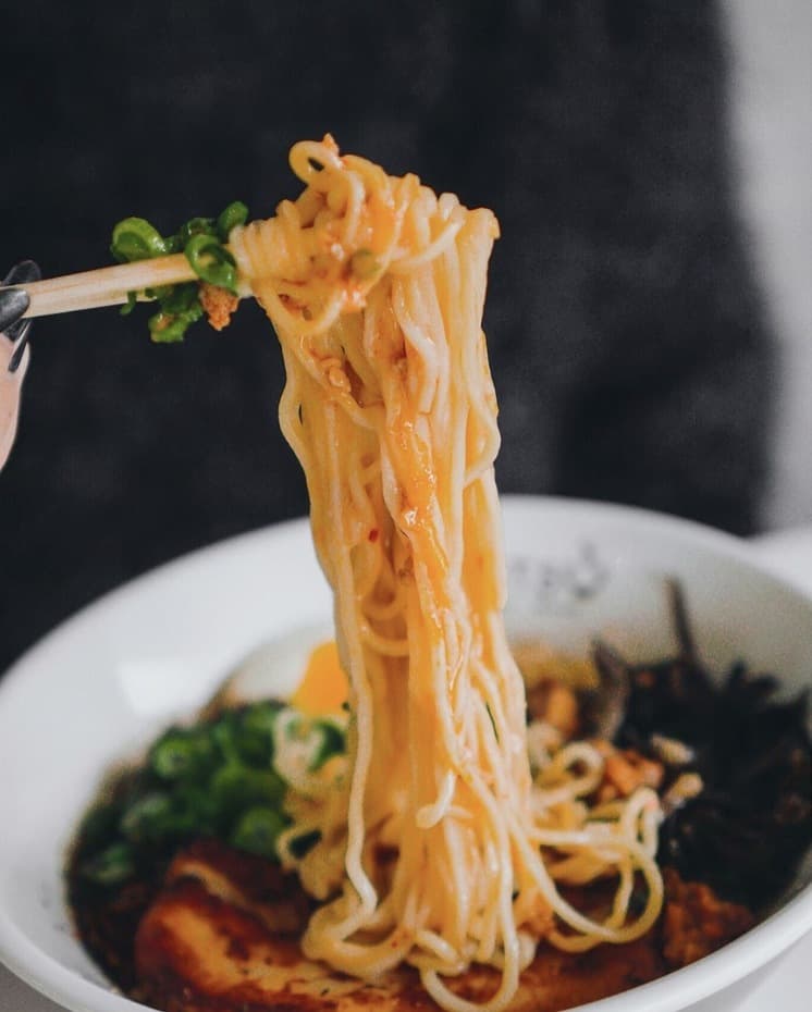 Ramen noodles lifted from a bowl with a jammy egg and pork